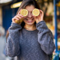 Person smiling at market holding up sliced lemons in front of their eyes