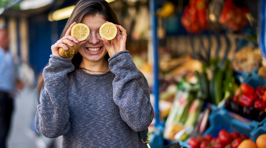 Woman smiling at food market holding sliced lemons in front of her eyes Woman smiling at food market holding sliced lemons in front of her eyes