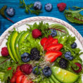Plate of salad topped with avocado and mixed berries