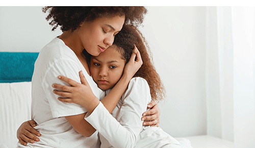 Mother hugging upset child on edge of bed