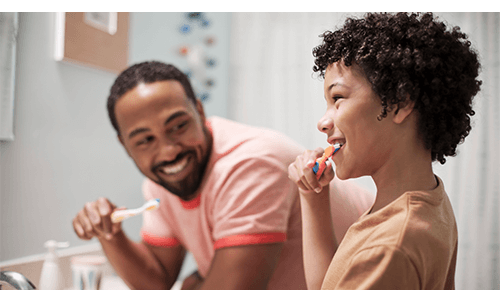 Father and child laughing while brushing teeth together in bathroom