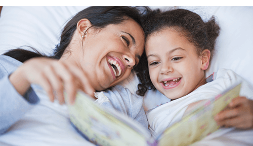 Mother and daughter reading together in bed at bedtime