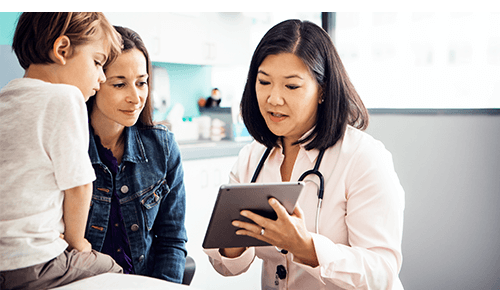 Mother and child in doctor's office talking to doctor and looking at digital tablet