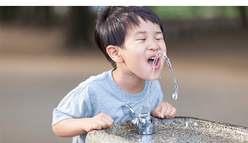 Child drinking water from a outdoor water fountain