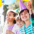Child wearing a birthday hat looking up at a balloon