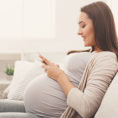 Pregnant person sitting on couch looking at a mobile phone