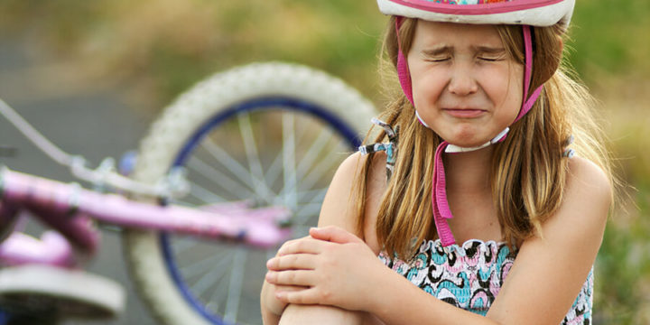 Young girl sitting next to bike crying and holding hurt knee