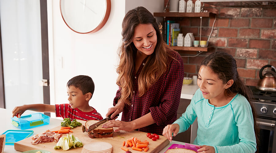 Mother and two children making lunch sandwiches together at kitchen countertop