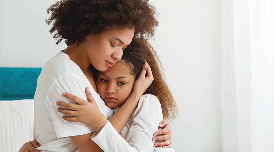 Mother hugging upset child sitting on bed