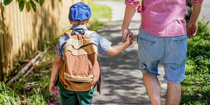 Parent and child with backpack holding hands while walking down a sidewalk together