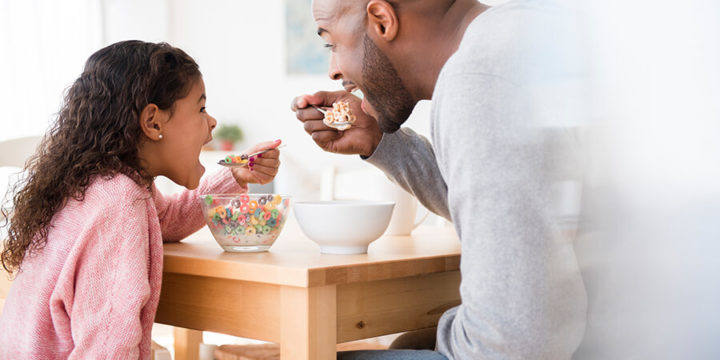 Father and child eating cereal together at kitchen table