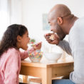 Father and child eating cereal together at kitchen table