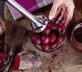 Person mixing beets in a bowl using hand blender