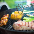 Closeup of tongs flipping vegetables and meat on a charcoal grill