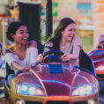 Two laughing young adults in a bumper car with another group in the background