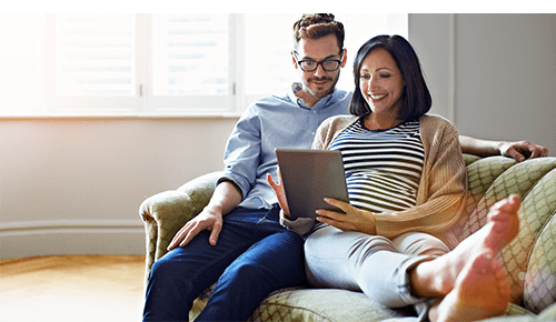 Couple sitting on couch looking at digital tablet together Couple sitting on couch looking at digital tablet together