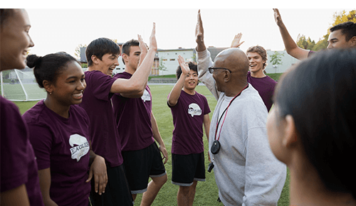 Group of teenagers and coach high-fiving during sporting event Group of teenagers and coach high-fiving during sporting event