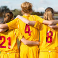 Back of group of teenagers hugging each other and wearing sports uniforms