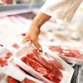 Person picking up a package of red meat from a grocery store display