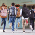 Group of children running down school hallway with backpacks on