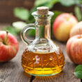 Small bottle of apple cider vinegar surrounded by apples