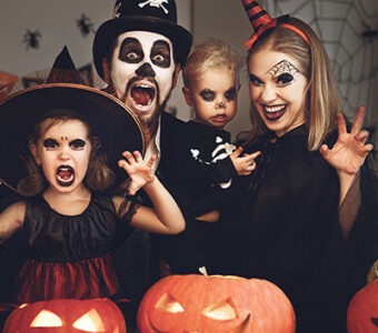 Family dressed up for Halloween and making funny faces in front of pumpkins
