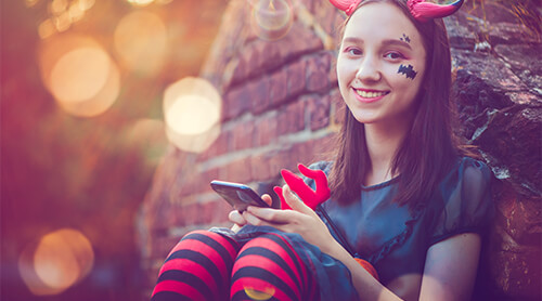 Teenager dressed in costume sitting outside with a mobile phone in hand, smiling at camera