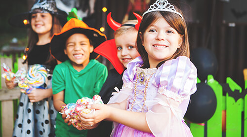 Group of children in Halloween costumers smiling at camera and holding candy
