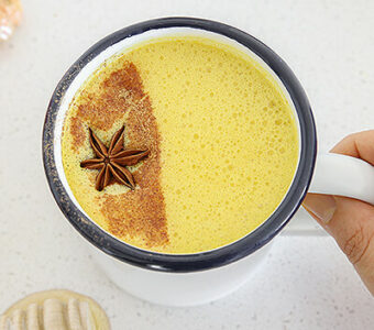 Mug of golden milk with spices on table next to it