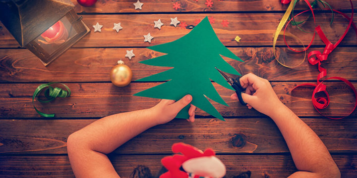 Child using scissors to cut a green tree from construction paper