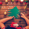 Child using scissors to cut a green tree from construction paper