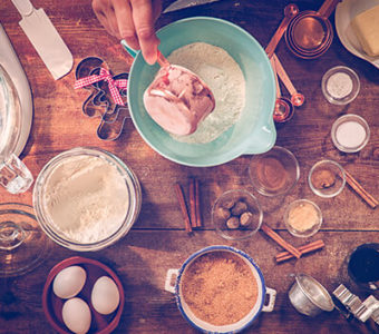 Birds-eye view of a kitchen countertop with baking supplies and accessories, while a person pours flour in a bowl