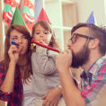 Parents and child celebrating New Year's Eve with noisemakers and wearing hats