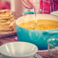 Person stirring a large pot of soup with grilled cheese sandwiches sitting next to it on the counter