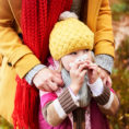 Child blowing their nose with a facial tissue while standing outside in front of an adult