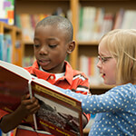 Two children looking at book together in library