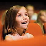 Child in awe gazing up at stage from theater seating