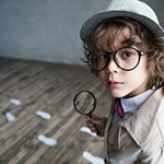 Young child wearing detective uniform and holding magnifying glass