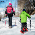 Adult and child walking on snow covered path wearing snow shoes