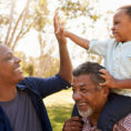 Three generations of family, grandfather with grandson on his shoulders while they walk outside