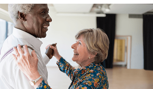 Two older smiling adults dancing together
