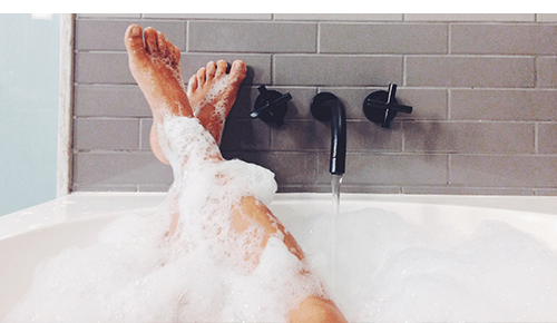 Closeup of feet up on the side of a bathtub during bubble bath