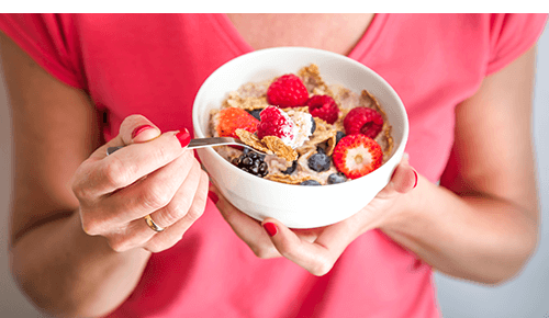 Person holding bowl of cereal and fresh fruit
