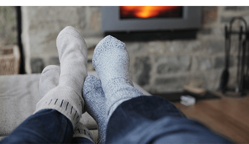 Two pairs of sock covered feet resting on couch in front of fireplace