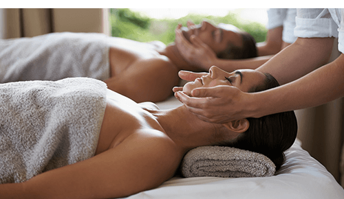 Two people receiving facial massages while laying on individual massage beds