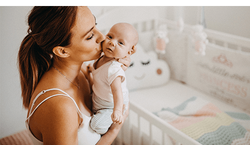 Woman kissing baby on cheek while holding it in nursery room Woman kissing baby on cheek while holding it in nursery room