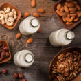 Birds-eye view of glass bottles filled with a variety of non-dairy milks with raw nuts sitting next to them