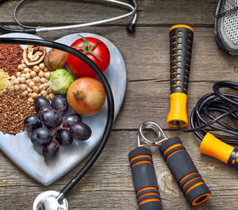 Heart shaped plate with grains, fruits and vegetables sitting next too workout equipment and a stethoscope