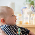 Person holding infant with bottles of milk and breast pump sitting in background