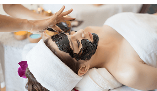 Woman receiving charcoal face mask at spa